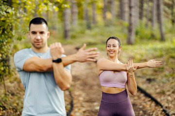 Selective focus on a sportswoman stretching arms in nature with her partner.