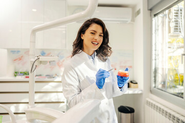 Portrait of a dentist smiling at the camera while holding a jaw model and talking about oral health.