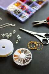 Box with colorful beads, string, wire, chain, scissors, pliers and hammer on dark background. Various jewelry making supplies. Selective focus.
