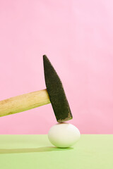 Hammer cracking white egg against pink studio background. Concept of Easter holiday, celebration,...