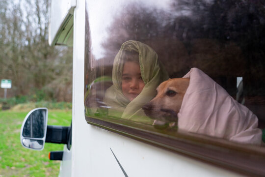 Boy with his dog wrapped up in duvets looking out of the window of a motorhome
