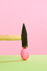 Hammer cracking painted pink Easter egg against pink studio background. Concept of Easter holiday,...