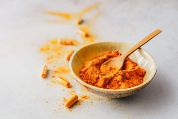 Kurkuma Pulver in einer Schüssel mit einem Holz Löffel auf einem grauen Tisch. 