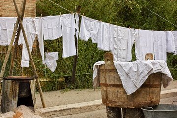 Ancient vat of laundry, brazier and old underwear and sheets hanging to dry. Laundry hung out, clothesline with ancient linen - 705634485