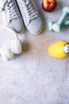 Sportschuhe, Kofph&ouml;rer, Wasserflasche und ein Apfel auf einem Beton Hintergrund. Draufsicht.