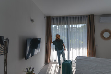 A young woman in a hat with a suitcase checks into a hotel room. Booking and Accommodation