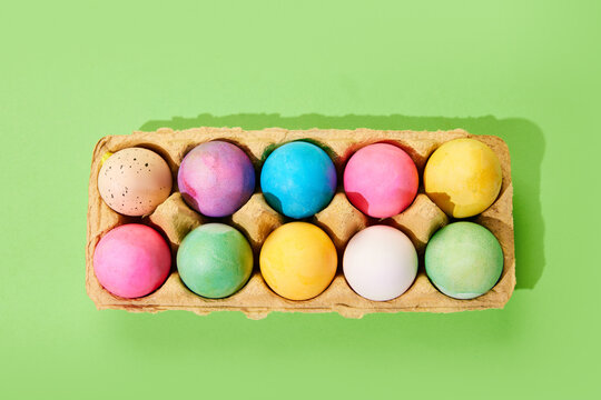 Multicolored painted Easter eggs on carton egg box isolated green background. Top view. Concept of Easter holiday, celebration, traditions, happiness. Postcard. Empty space for ad