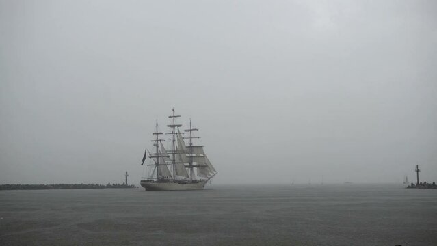 A sailship goes to sea during a rain. 
A sailing ship leaves the harbor during a rain