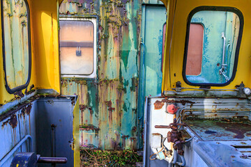 Interior of very old railway cockpit without doors, metal walls corroded, peeling and rusty from passage of time of a passenger car in the background