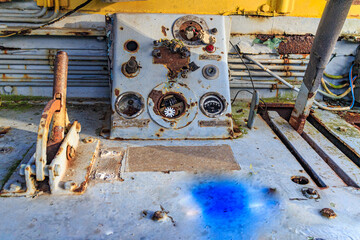 Small control panel and levers inside a very old dismantled railway cockpit, metal corroded and rusted by passage of time, cables, gray painted metal and peeling yellow in background