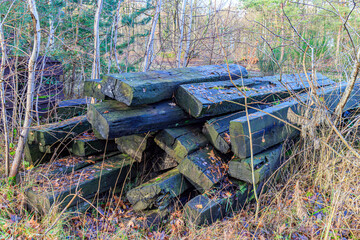 Old disused railway sleepers stacked between wild vegetation and bare trees in background, surroundings of old train station, sunny day in As, Limburg, Belgium