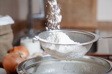 White flour is poured into a sieve over a bowl....