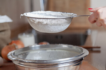 A woman hand holds sieve with flour over a bowl....