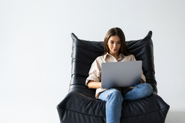 Relaxed young woman sitting in a bag chair with stretched arms using a laptop