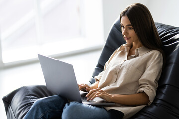 Relaxed young woman sitting in a bag chair with stretched arms using a laptop