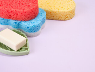 White natural soap lies on a soap dish in the shape of a green leaf. The red, blue and yellow shower sponges are on the table. Copy space for text.