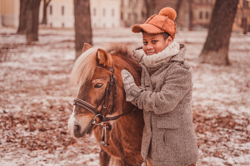 the boy hugs the pony and strokes her neck while looking at the camera