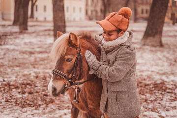 the boy hugs the pony and strokes her neck while looking at the pony