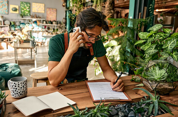 Service and shopping concept. Handsome caucasian man in eyeglasses and apron making notes on...
