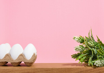 Raw chicken white eggs in a cardboard container on a pink background. Copy space for text. Green...
