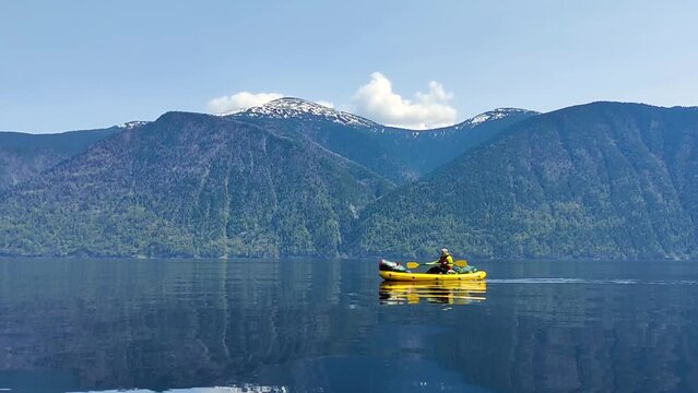 Alone man on kayak boating in Siberian Teletskoye Lake. Calm spring weather, reflection of canoe on a bit ripple water.