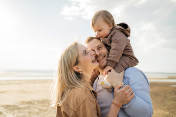 Happy family enjoying a beach day, with toddler on father's shoulders, sharing a moment of joy.