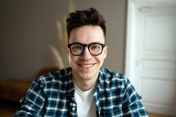 Smiling young man with glasses in a plaid shirt, exuding confidence and approachability indoors.