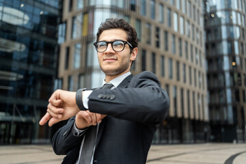 Young businessman checking time on his watch, standing confidently in an urban business district.