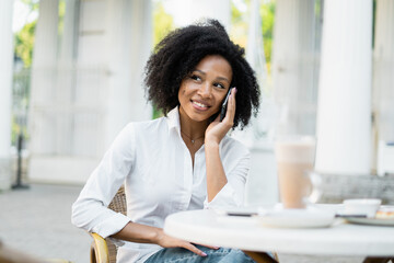 Radiant woman enjoying a conversation on her smartphone at an outdoor cafe.