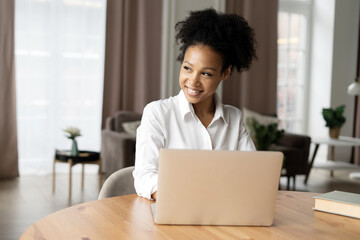 Joyful woman working on laptop with a bright smile, feeling accomplished in a cozy home setting.