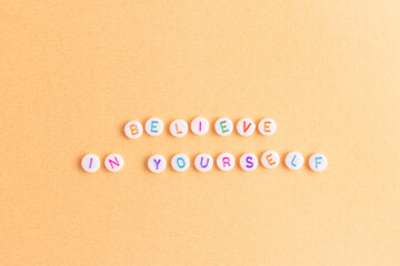 Believe in yourself. Quote made of white round beads with multicolored letters on a golden...