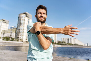 Active man performing a stretch routine along a river promenade with urban skyline.