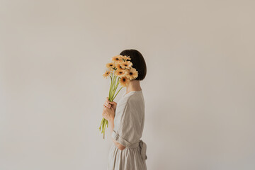 Gerbera flowers bouquet in female hands. Young pretty woman in neutral tan sandy beige linen dress