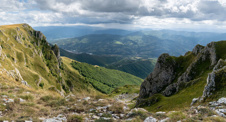 Mountain view from Vlasic near Travnik, rocky slopes overgrown with grass in sunlight and hazy mountains in distance during cloudy day
