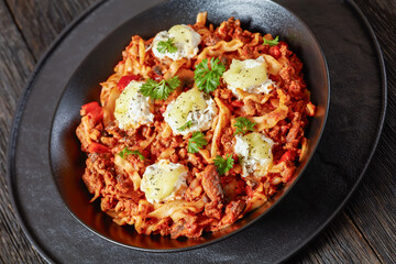 close-up of Lasagnette with beef ragu, mushrooms and ricotta cheese in black bowl on dark wooden...