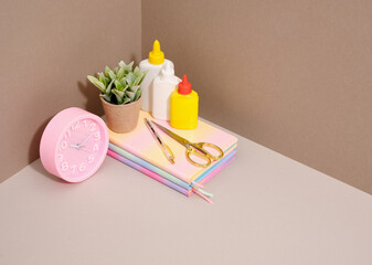 Collection of school supplies on table. Pink clock and glue, colored notebooks, stationery.