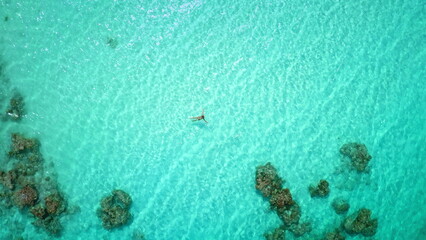 Top down view person swimming crystal turquoise sea water. Female in bikini relax and enjoy outdoor lifestyle travel on summer holiday vacation. Explore coral reef underwater life. Aerial drone shot