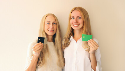Portrait of happy smiling caucasian middle aged mother or sister and adult daughter holding plastic credit bank card together on studio background - obrazy, fototapety, plakaty