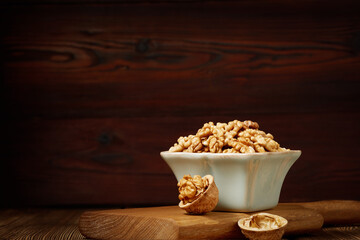 A bowl of peeled walnut kernels on a wooden board with copy space.