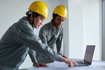 Team of construction workers in overalls and hardhats checking building blueprint