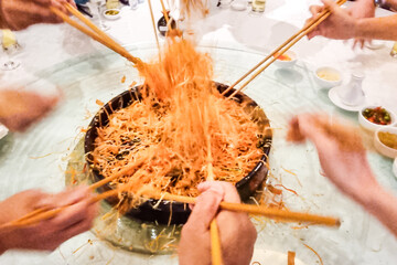 People mixing and tossing yusheng or yee sang during Chinese New Year dinner celebration. Slow shutter speed with motion blur intended. - obrazy, fototapety, plakaty