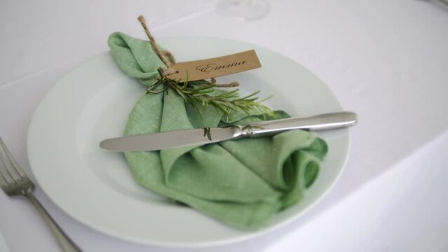 Place-card with the name Emma on a place-card. A plate with place-card Emma and a green napkin. Seats for. Place at the banquet for. Serving the place-card for Emma.