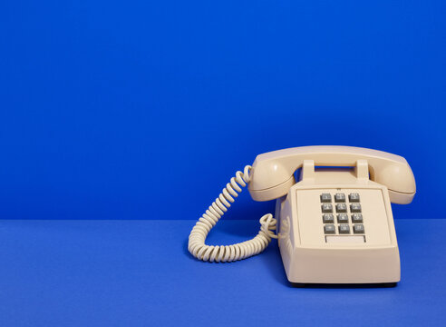 Beige retro phone with gray buttons on a blue background. Copy space for text.