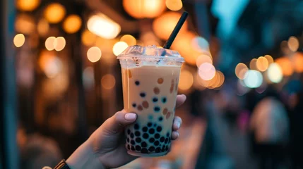 Foto op Plexiglas Female hand holding Bubble tea Asian sweet cold tapioca pearls drink night city. © okfoto