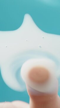 Vertical video. A man's hand spreads a white viscous liquid on the glass with a finger against a blue background, possibly a cleaning agent. Low angle view focus on window