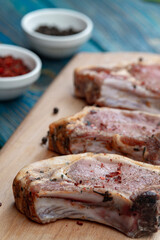 Raw pork ribs with spices and herbs on cutting board on wooden background