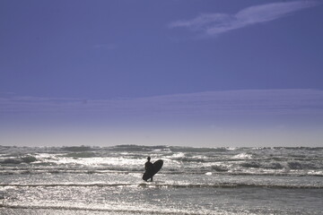 Man with surfboard stands on the beach and looks at the waves