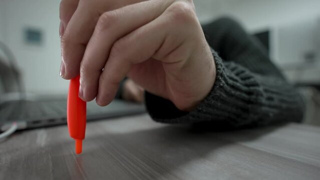 Close-up of tapping ballpoint pen on desktop. Man thoughtfully taps his pen on table next to laptop. Office worker thinks while working at computer. The man clicks his pen on table.