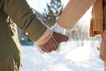 Close-up of hands in mittens and gloves and warm winterwear of affectionate couple standing in...