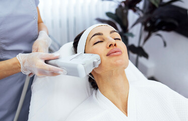 Portrait of relaxed young female client getting SMAS ultrasound face lifting massage